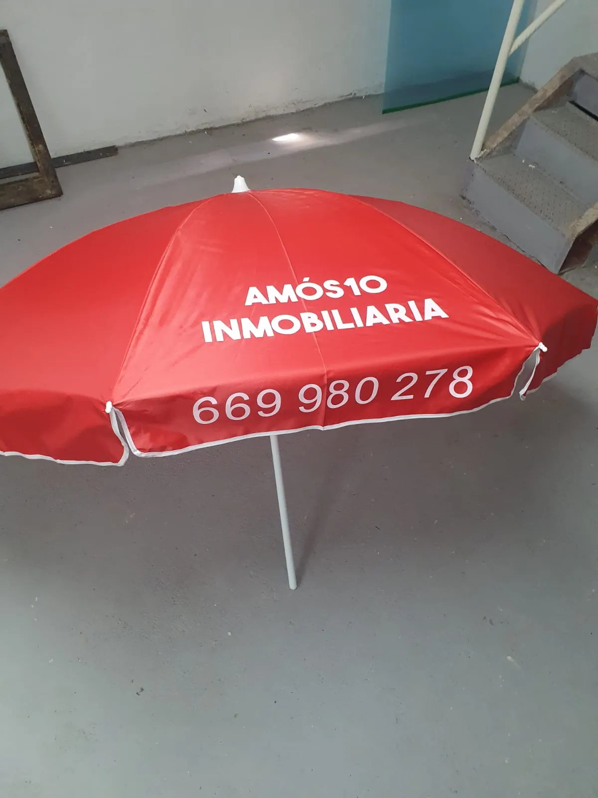 Sombrilla publicitaria de Amós 10 Inmobiliaria con el teléfono de contacto